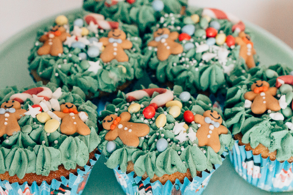 Christmas tree cupcakes with piped decoration and adorned with candy canes, baubles and mini gingerbread men.
